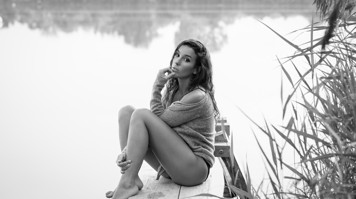 looking at viewer, monochrome, girl, reflection, pier, nature, legs, sweater, hand on face, brunette, model, girl outdoors, grass, water, lake