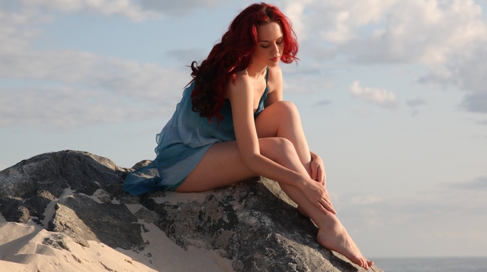girl, girl outdoors, bare shoulders, redhead, sea, looking down, long hair, sitting, blue dress, model, barefoot, rock, sand, clouds