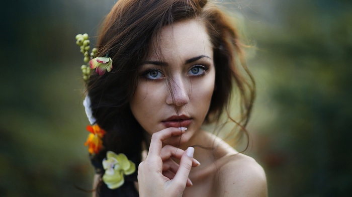 blue eyes, bare shoulders, brunette, girl outdoors, depth of field, hand on face, flower in hair, looking at viewer, flowers, girl, face